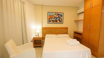 Een hotelkamer met een bed, een stoel, een nachtkastje, een schilderij aan de muur en een kledingkast.