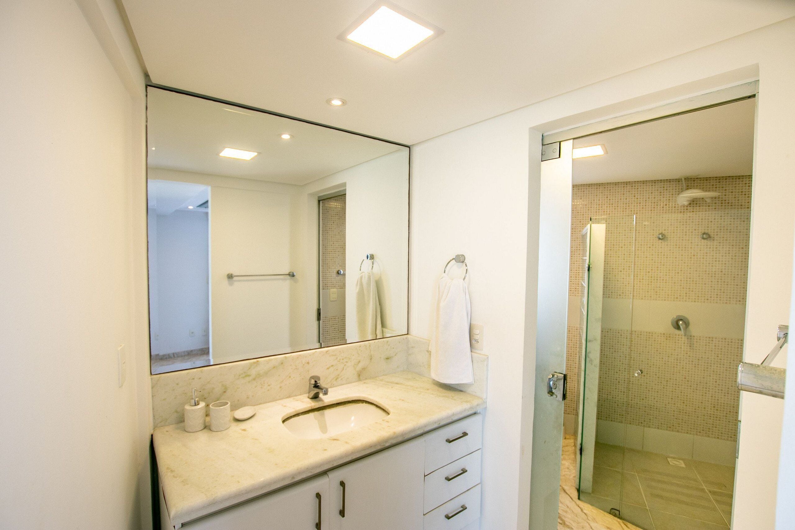 A bathroom with a marble sink, a large mirror, a glass shower enclosure, and a towel rack.