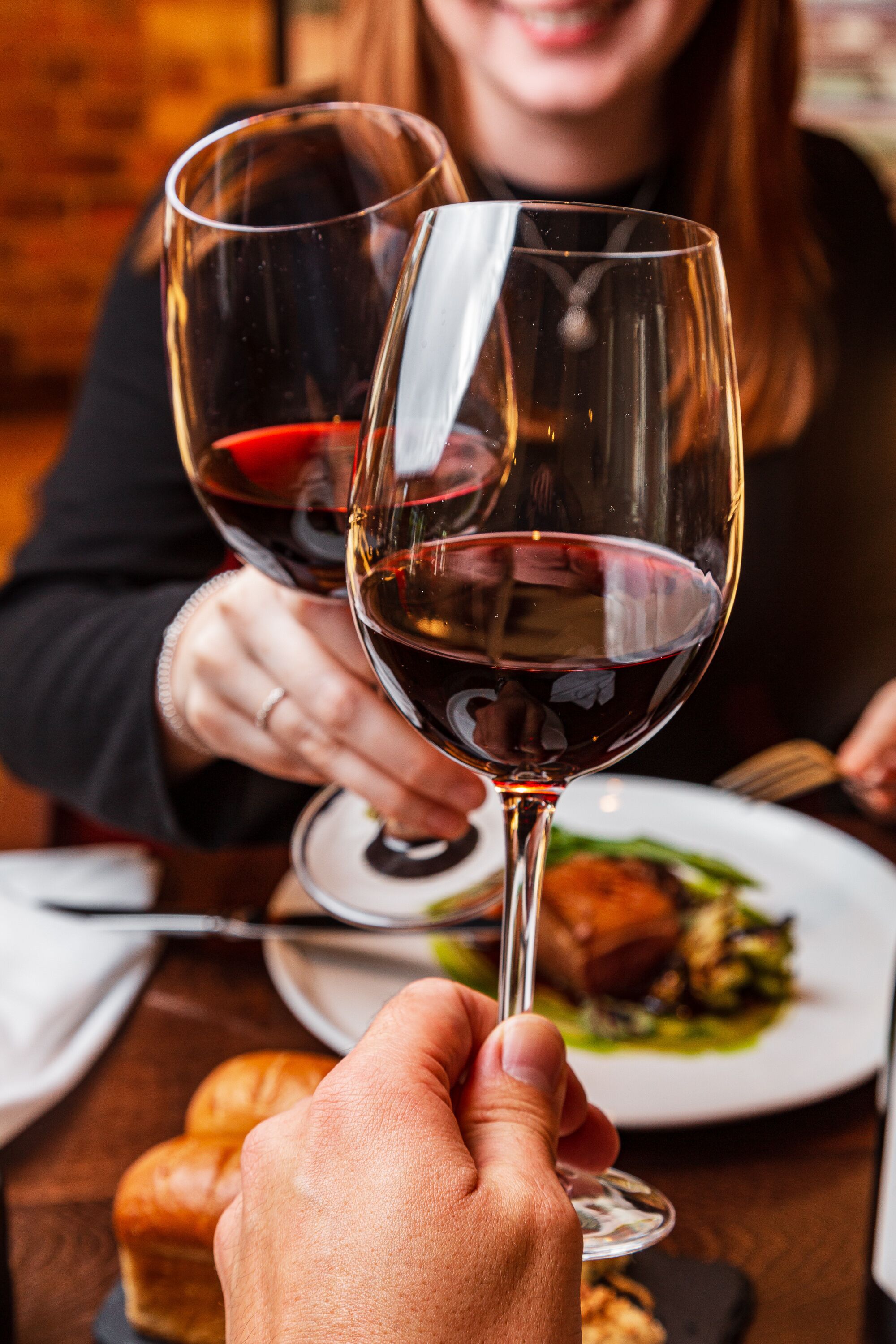 A person holding two wine glasses with a plate of food in the background.