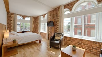A modern hotel room with exposed brick walls, a large bed, a desk, and a TV mounted on the wall.