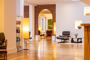 A spacious lobby with a wooden floor, a brick archway, and a seating area with leather chairs and a glass table.