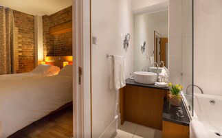 Habitación de hotel con pared de ladrillo, una cama, baño con lavamanos, espejo y bañera.