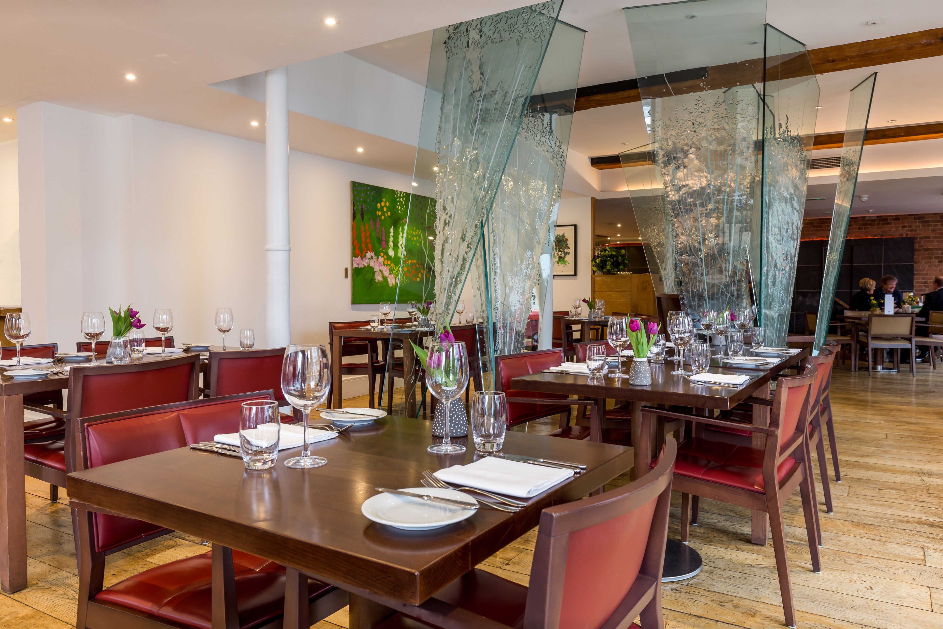 A dining area with multiple tables set for service, featuring glass partitions and red upholstered chairs.