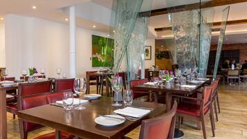 A dining area with multiple tables set for service, featuring glass partitions and red upholstered chairs.