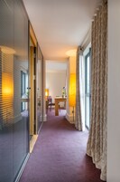 A hotel hallway with a purple carpet, a dining area with a table and chairs, and a large window with curtains.