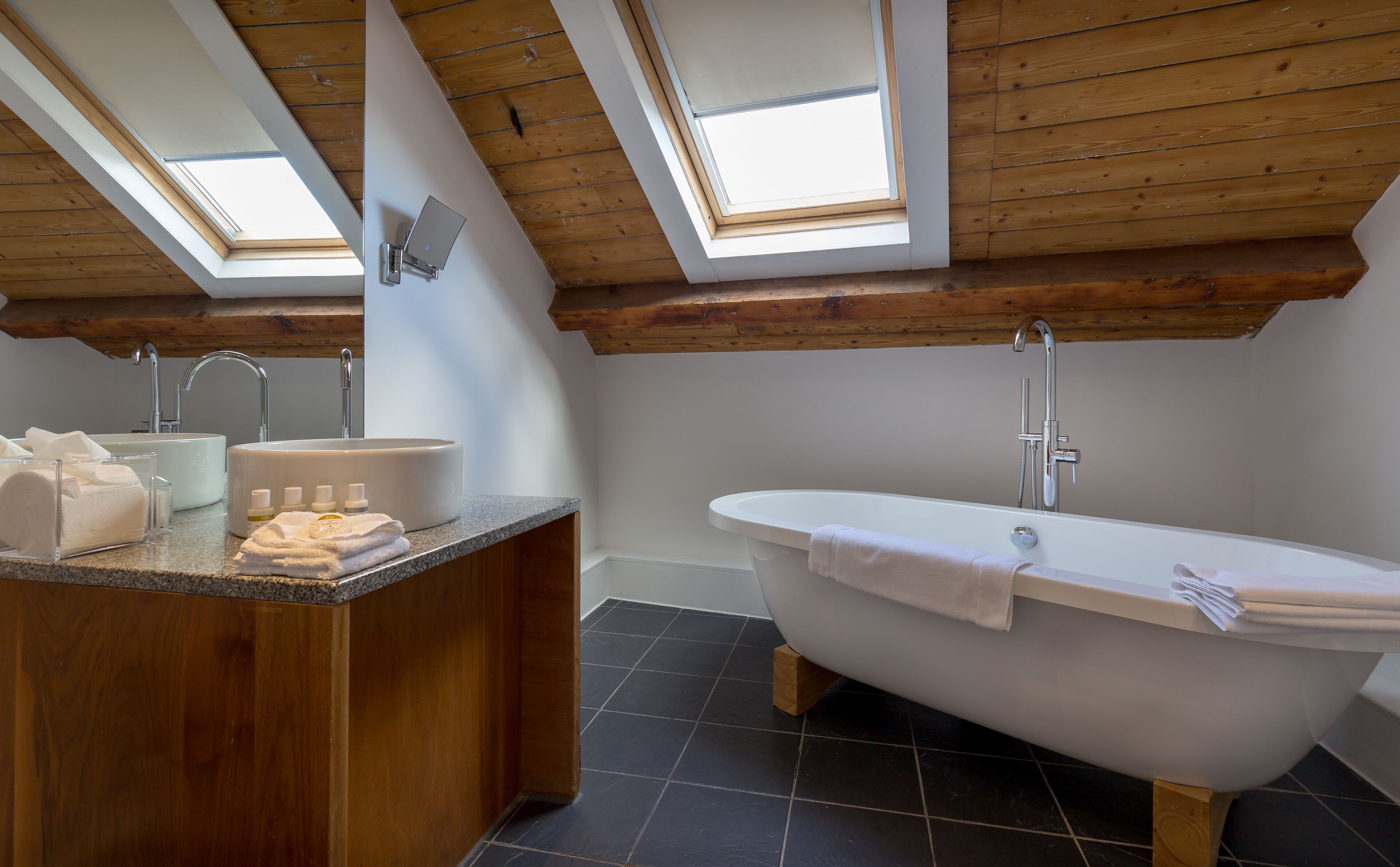 Un baño moderno con tragaluces, una bañera independiente y un tocador de madera.