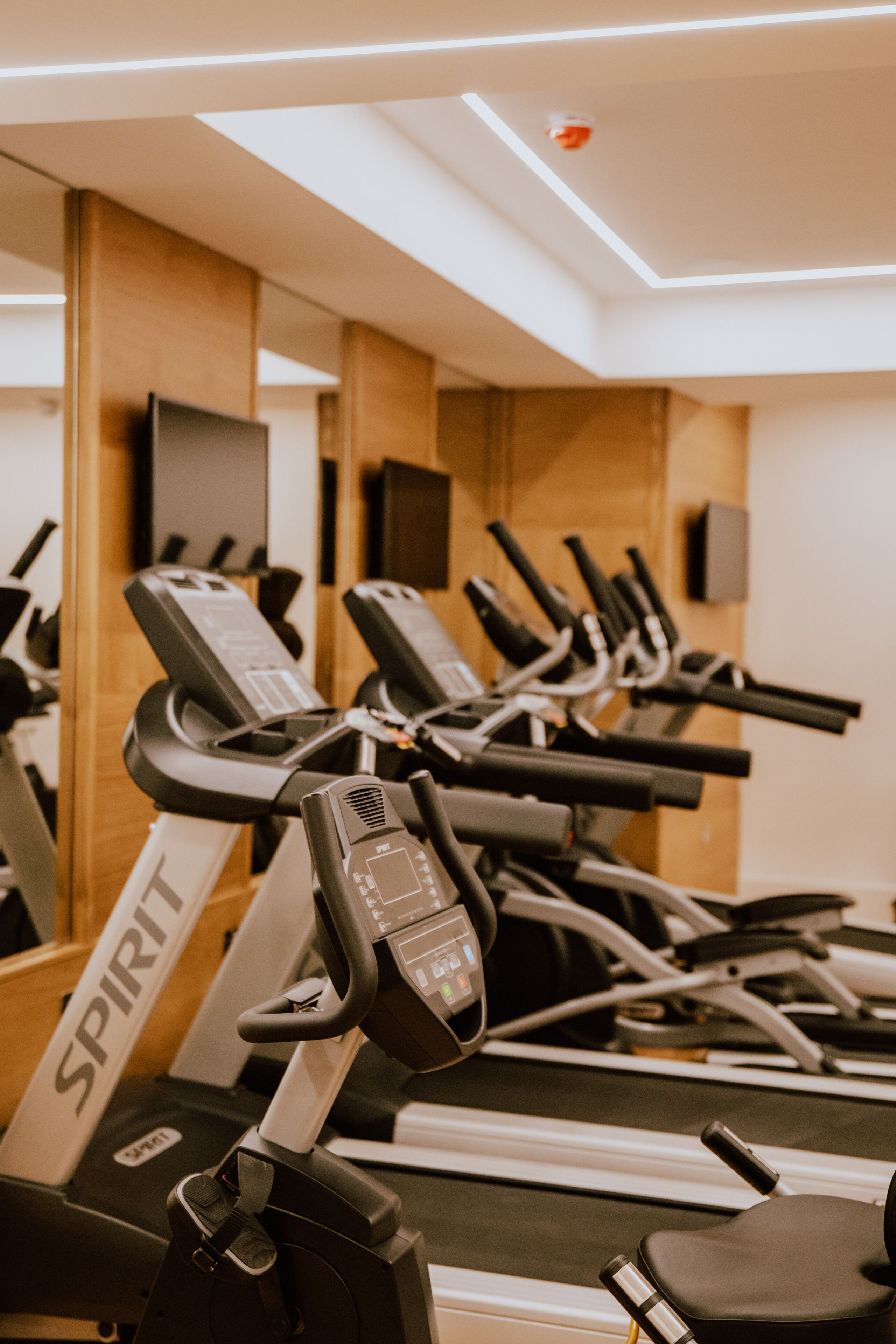 A row of stationary bikes in a gym with a wooden wall and a ceiling light fixture.