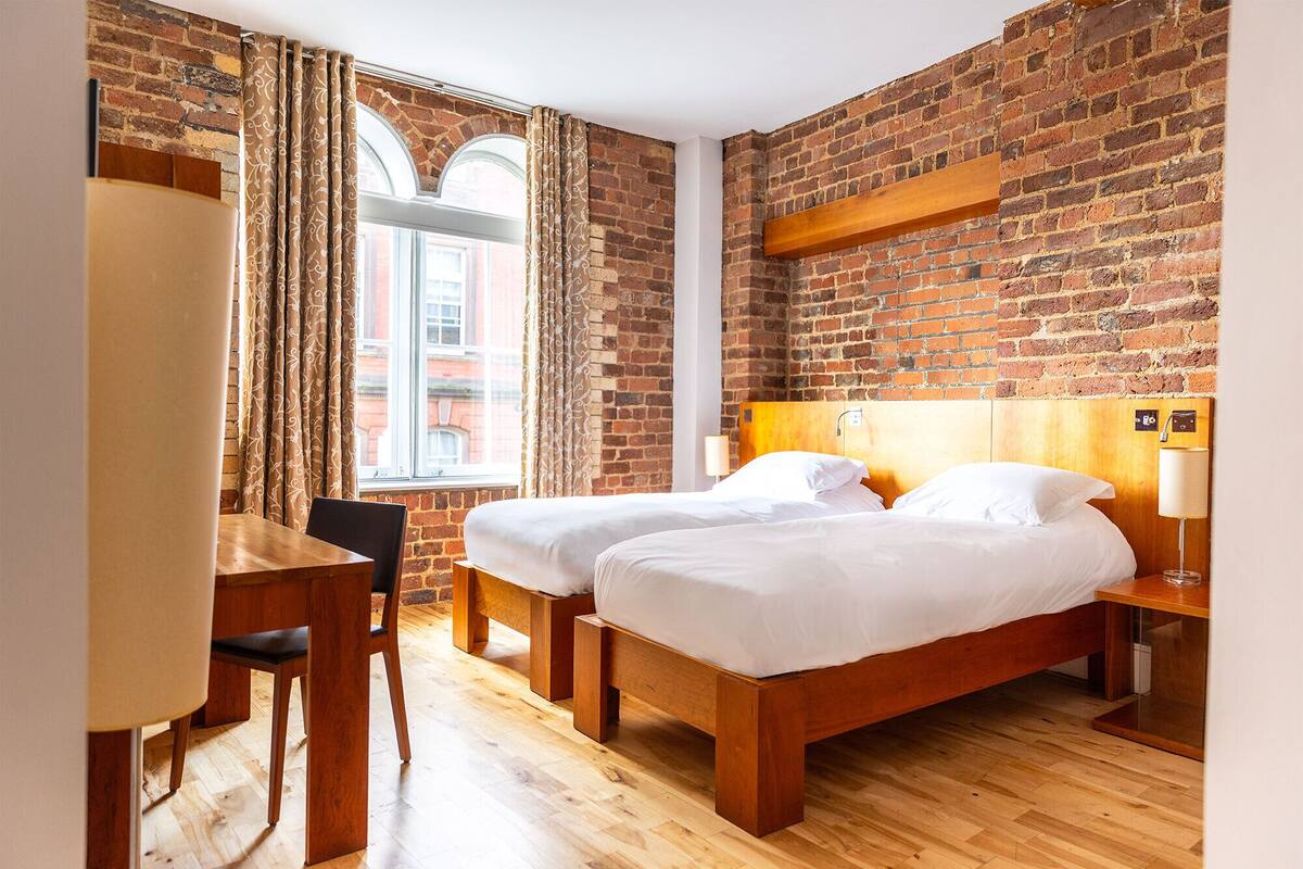 A hotel room with two wooden beds, a desk, and a chair.