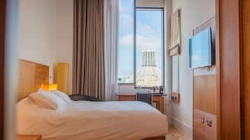 A hotel room with a bed, a desk, a chair, a TV, and a window with a cityscape view.