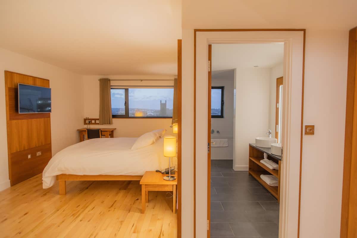A bedroom with a bed, bedside table, lamp, and a TV mounted on the wall.