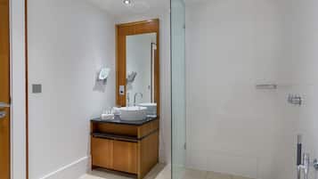 Un baño moderno con un tocador de madera, un espejo grande, un lavamanos blanco y una zona de ducha con mampara de vidrio.