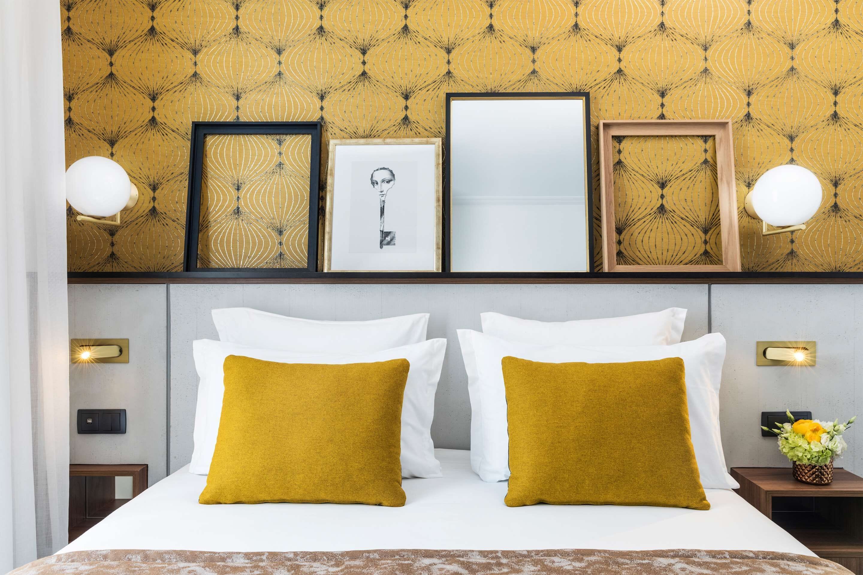 A hotel room with a bed, white pillows, mustard-colored accent pillows, a headboard, and framed artwork on the wall.
