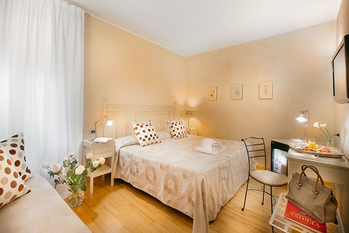 A hotel room with a bed, bedside table, chair, and a desk with a chair.