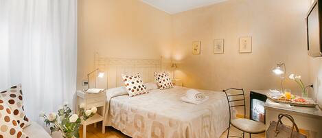 A hotel room with a bed, bedside table, chair, and a desk with a lamp.