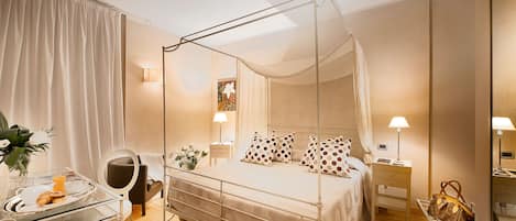 A four-poster canopy bed with a bedside table and lamp, a chair, and a small desk with a tray of croissants.