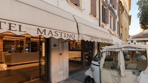 A hotel entrance with a canopy labeled "Hotel Mastino," a reception desk, and a vintage car parked outside. - Hotel Mastino (Verona)