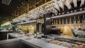A bar area with shelves of liquor bottles, a glass display case with pastries, and hanging wine glasses. - Hotel Mastino (Verona)