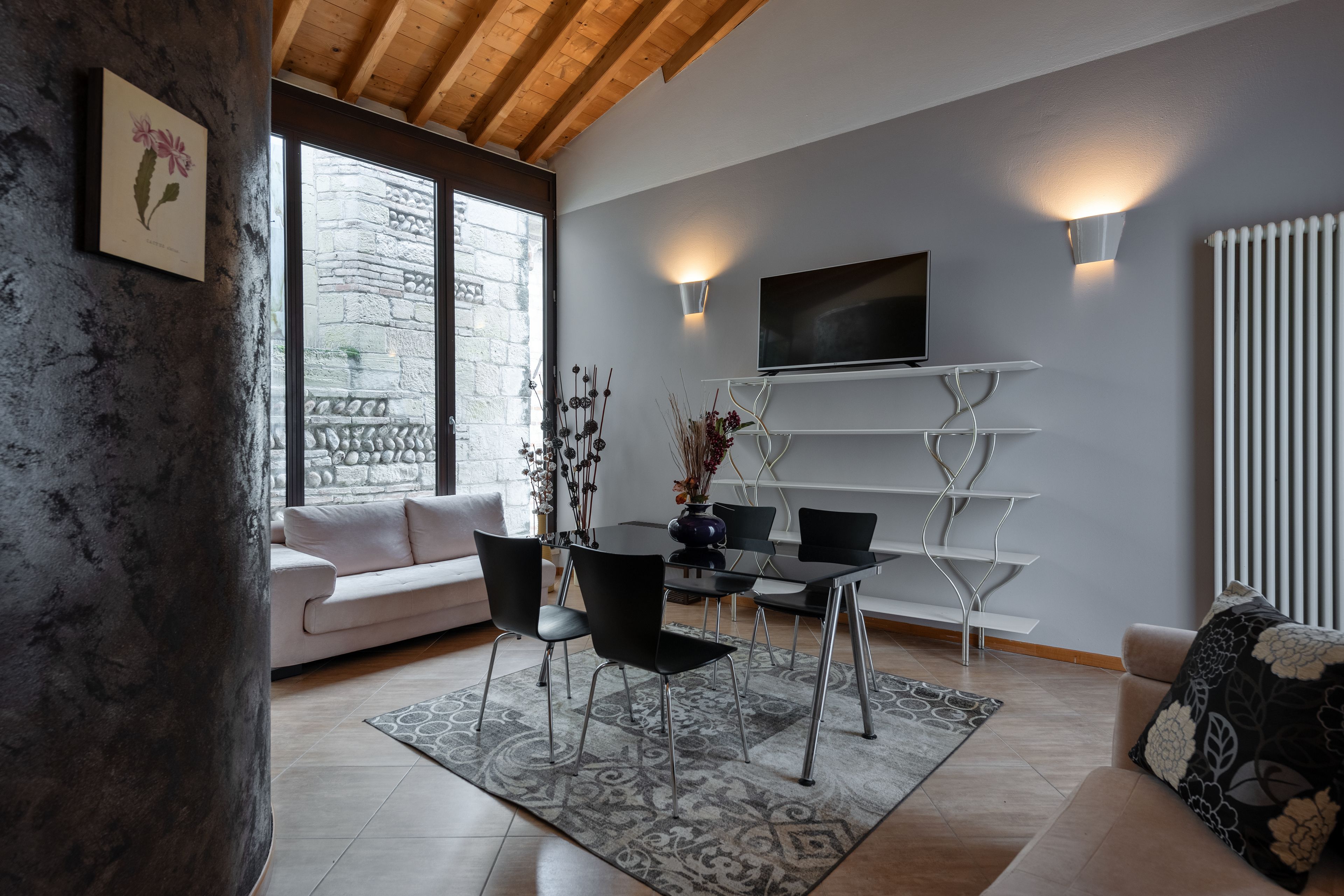 A modern living room with a white sofa, black chairs, a dining table, and a TV mounted on the wall.