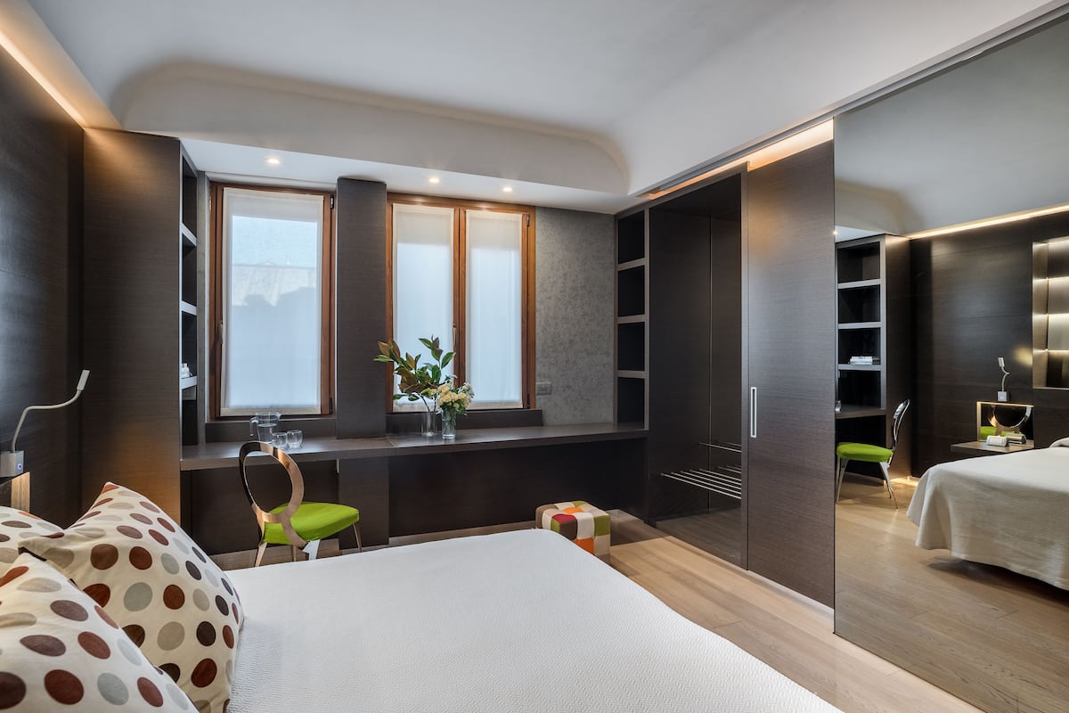 A modern bedroom with a bed, a desk with a chair, a wardrobe, and a window with a view.