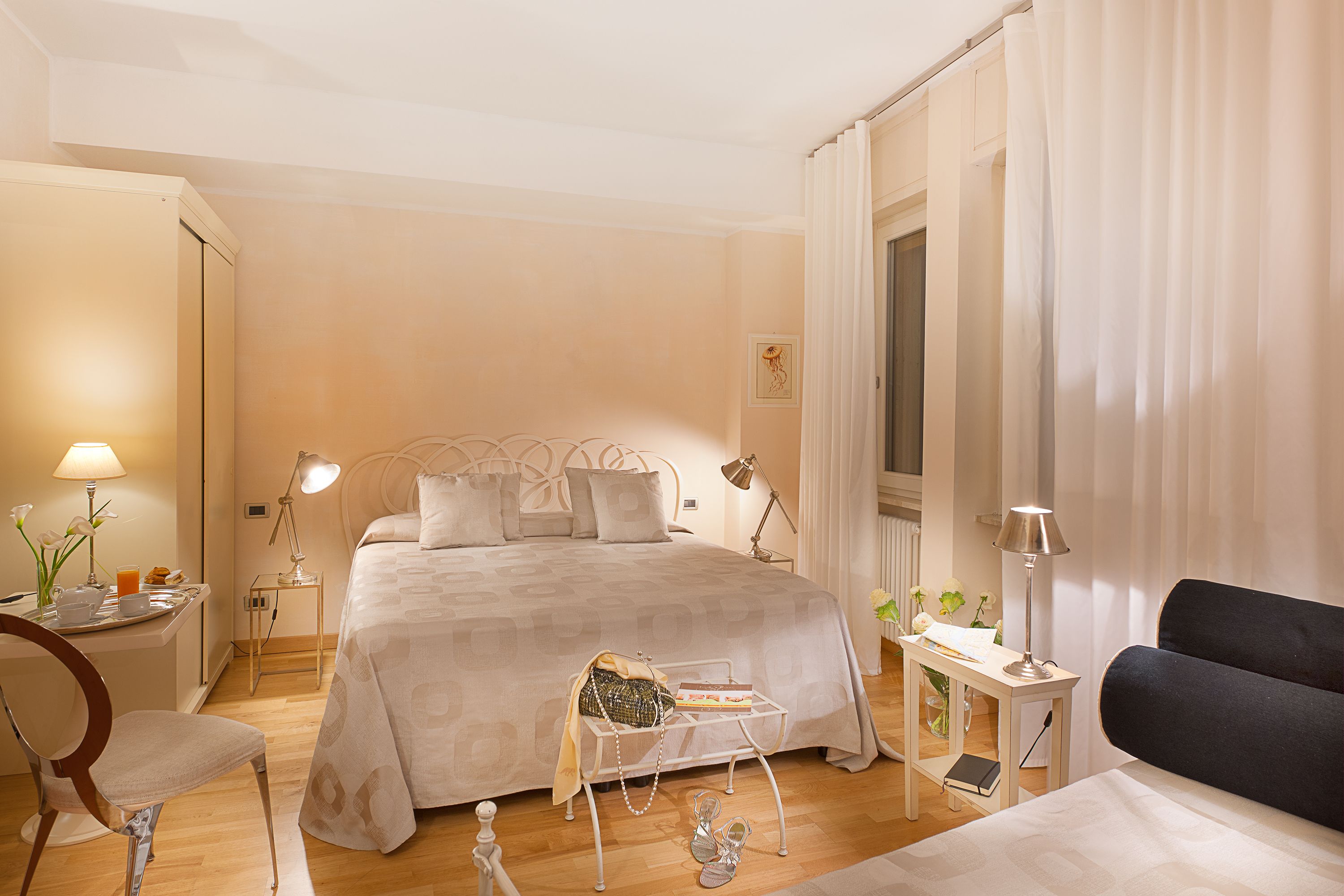A well-lit bedroom with a large bed, bedside tables, a chair, and a desk with a lamp.