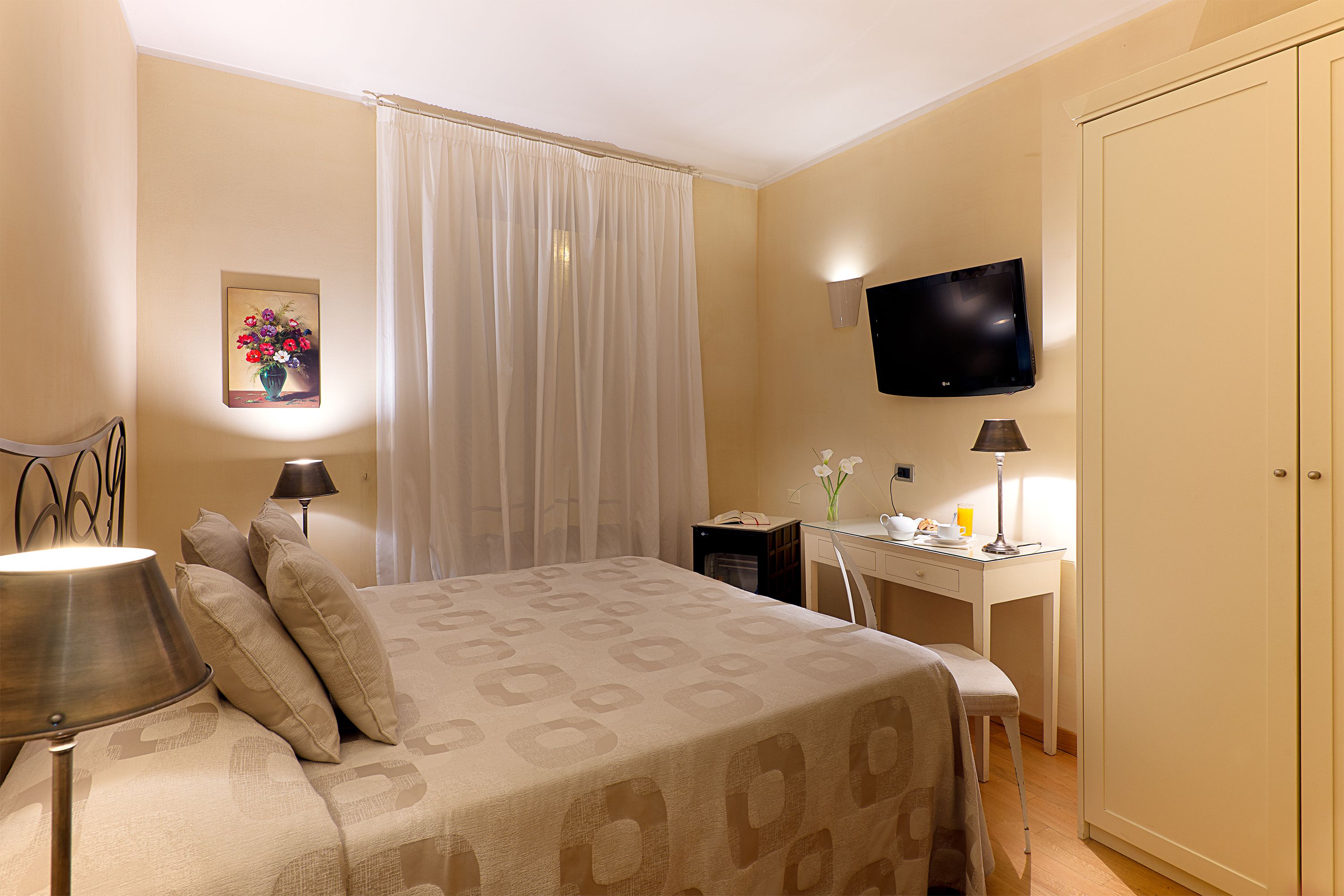 A hotel room with a bed, desk, TV, and a wardrobe.