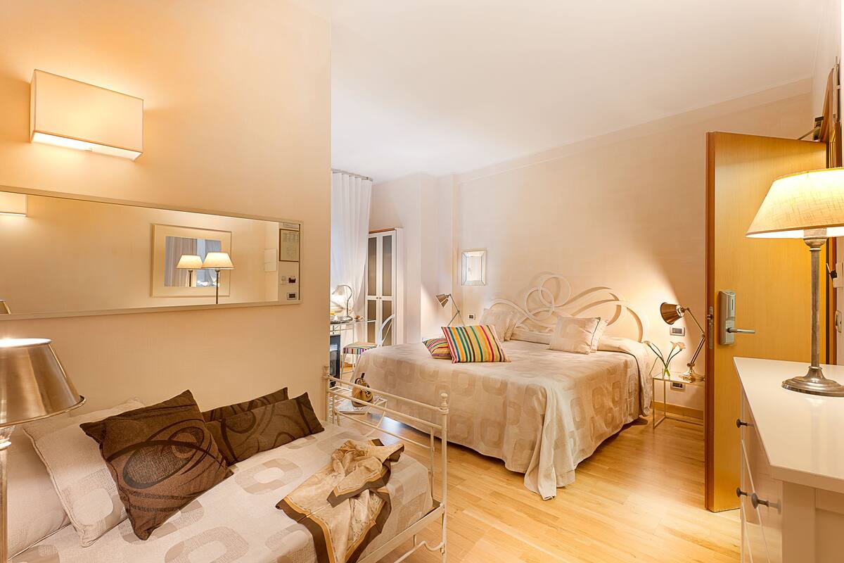 A hotel room with a bed, a sofa, a desk, and a mirror.