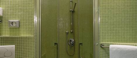 Une salle de bain avec des murs recouverts de carreaux verts, une douche en verre, des toilettes et un lavabo, avec une serviette accrochée au mur.