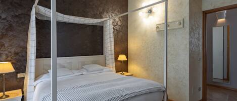 Una cama con dosel, una mesita de noche con lámpara, y una lámpara de pared.