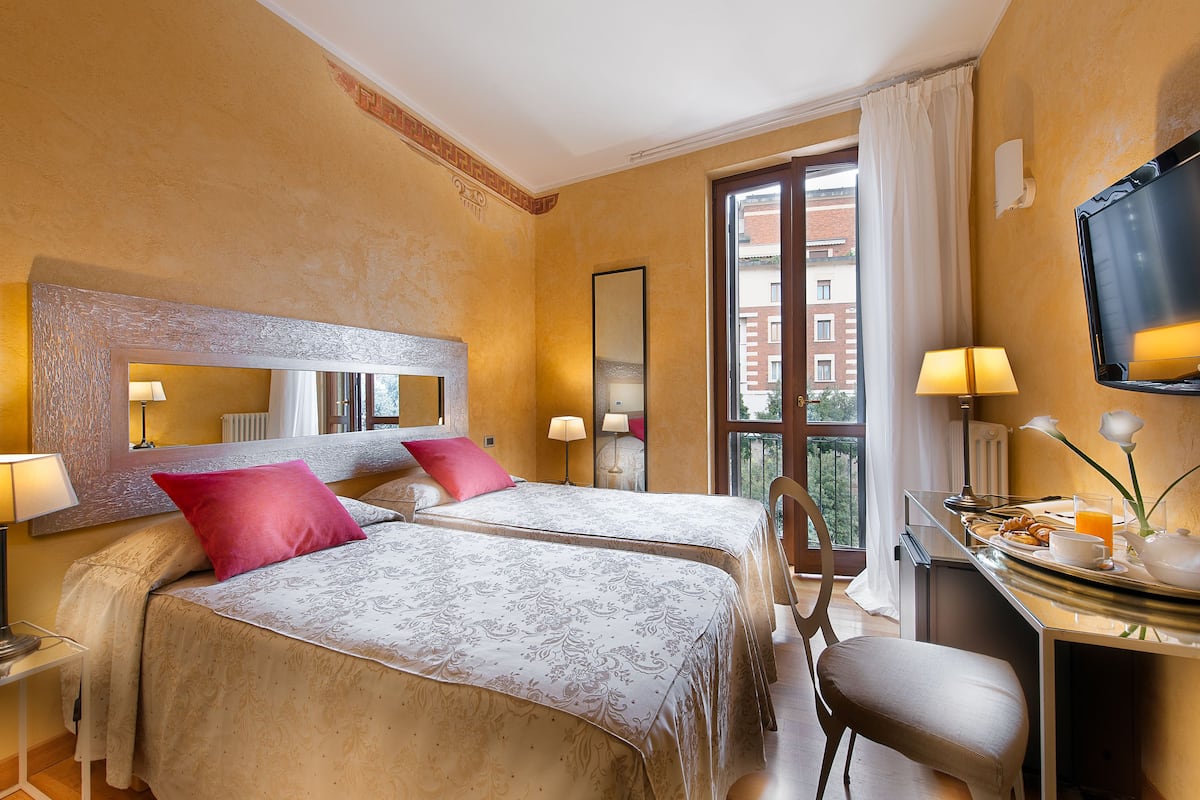 A hotel room with two beds, a desk with a chair, a TV, and a window with curtains.