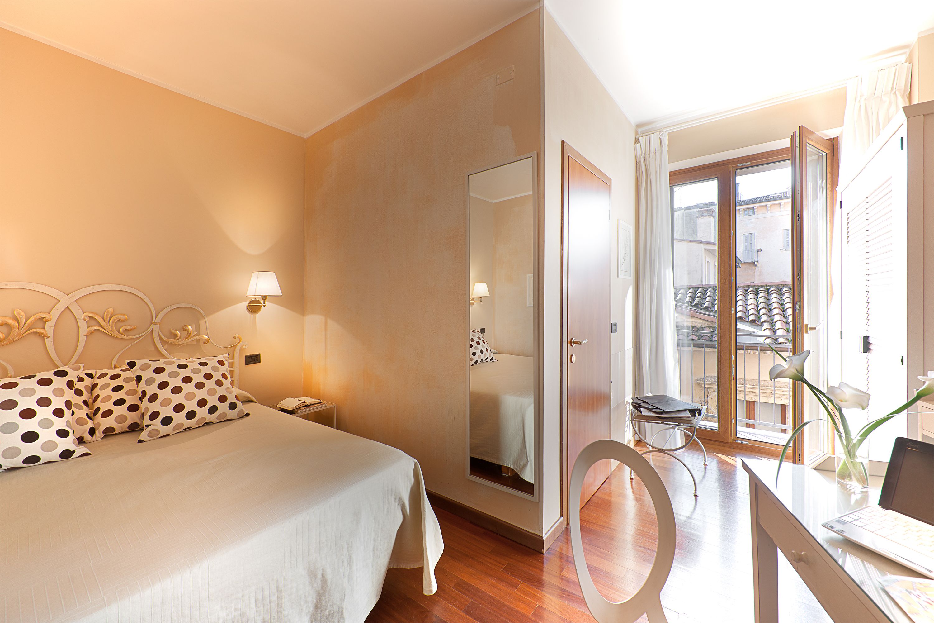 Habitación de hotel con cama, lámparas de noche, un escritorio con una computadora portátil y vistas al balcón exterior.