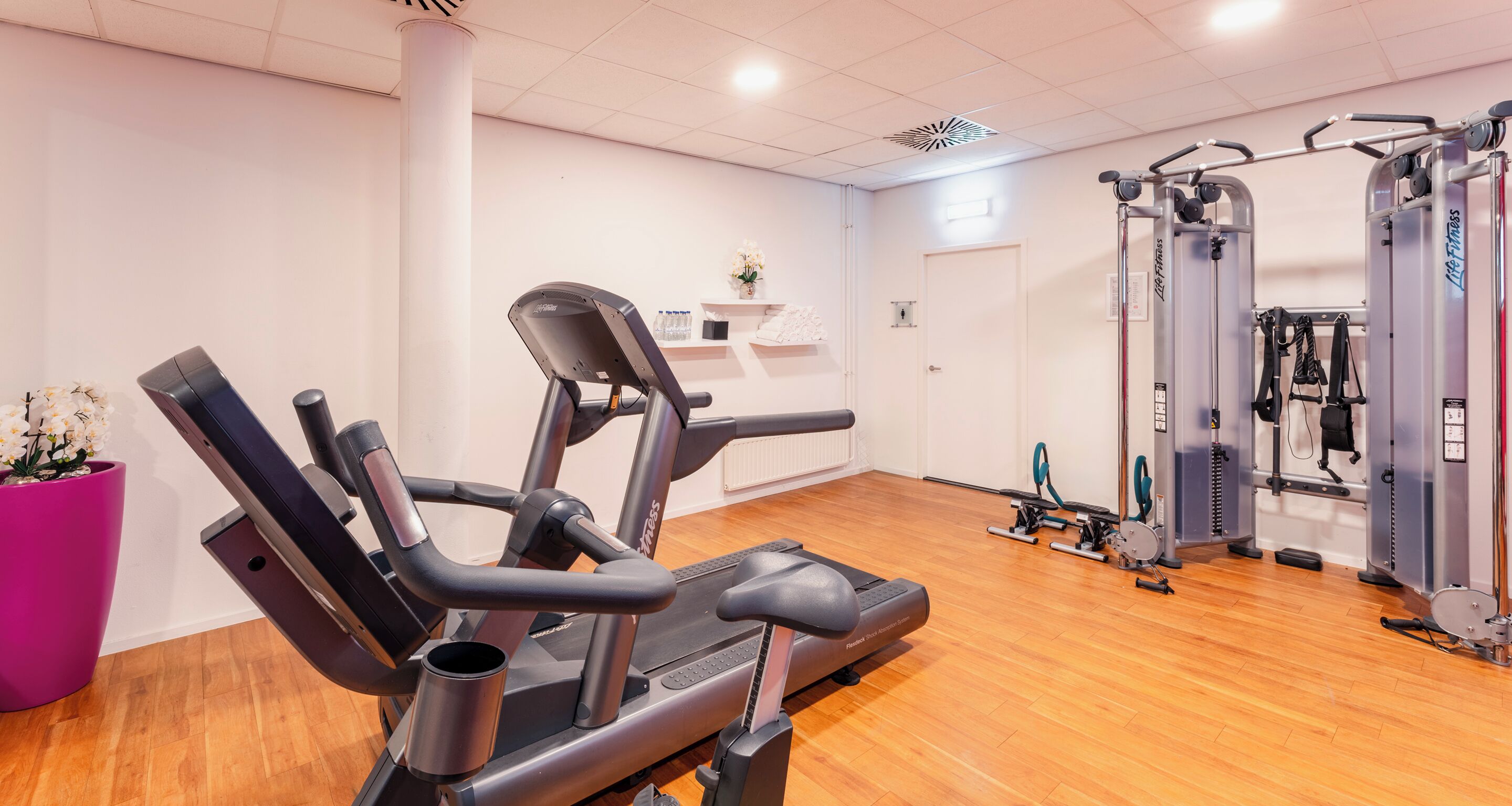 Ein Fitnessstudio mit Cardiogeräten, Krafttrainingsgeräten und Holzboden.
