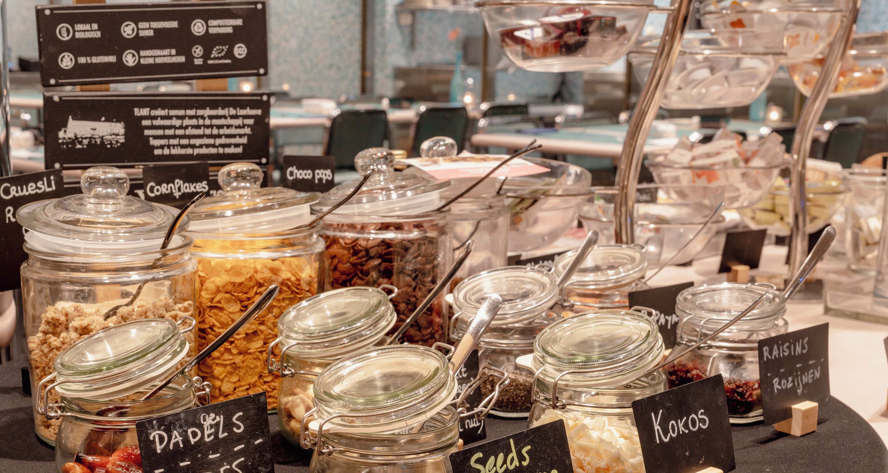 Ein Buffet mit verschiedenen Speisen, darunter 'Cakes', 'Cornflakes', 'Choco pops', 'Rosinen', 'Kokos' und 'Samen'.