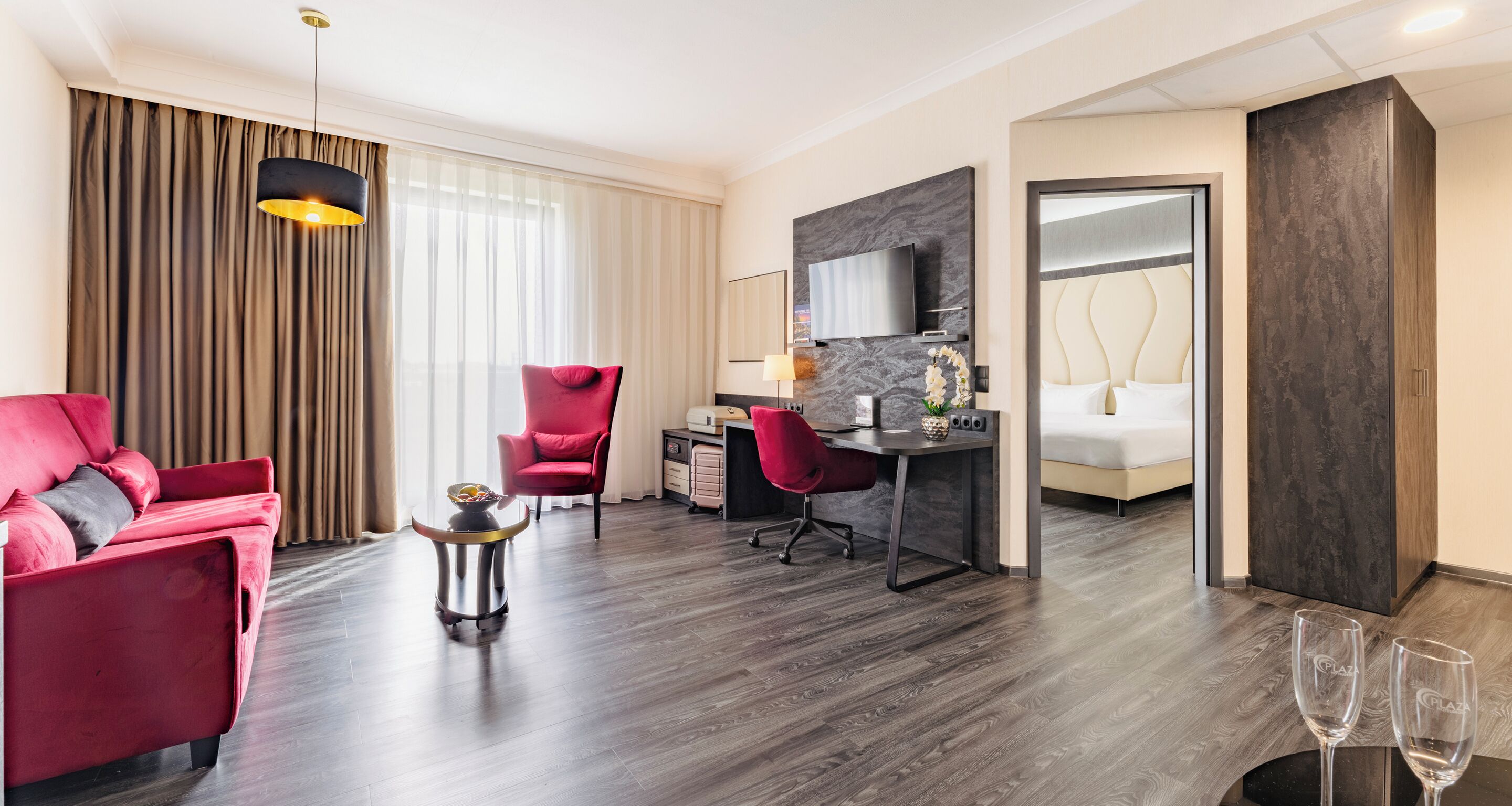 Een moderne hotelkamer met een rode bank, een bureau met stoel, een bed, een televisie en een minibar.