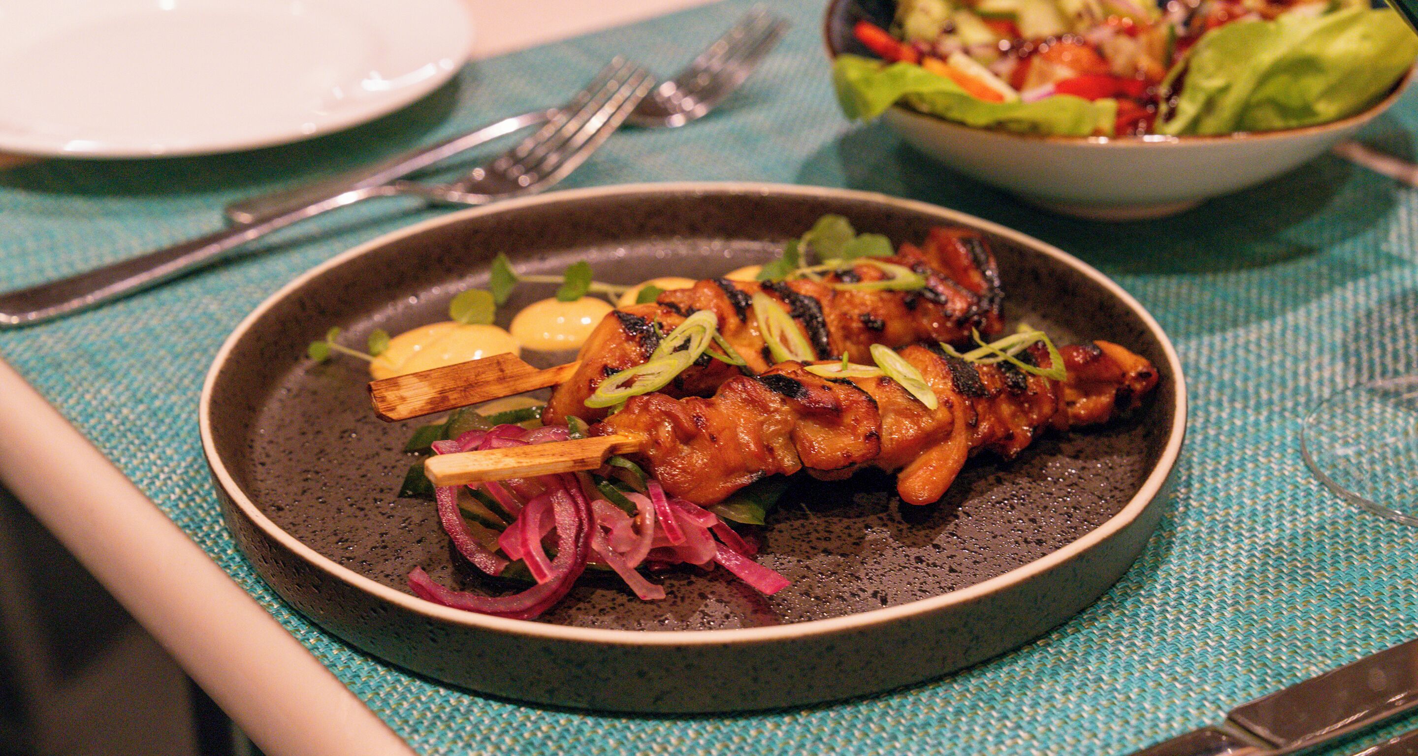 A plate of grilled chicken with vegetables on a textured tablecloth.