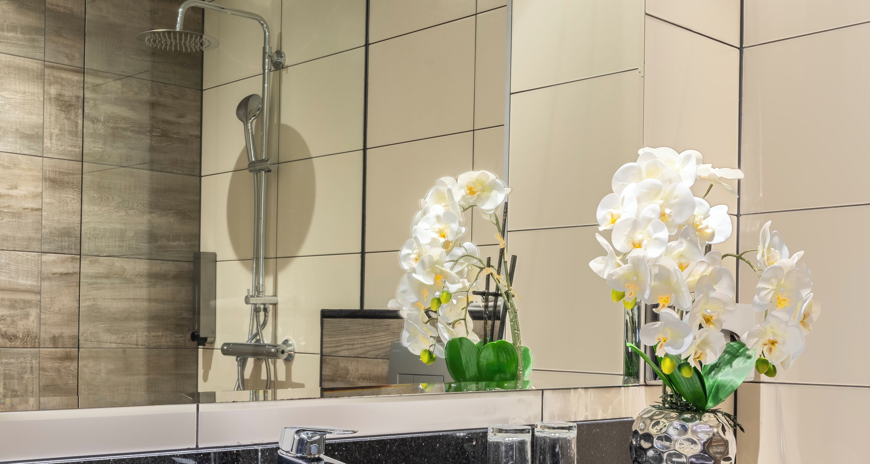 Une salle de bain avec une douche, un miroir et un vase contenant des orchidées blanches.
