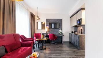 Una habitación de hotel moderna con un sofá rojo, una mesa de comedor con sillas, una zona de cocina y un televisor de pantalla plana grande montado en la pared.