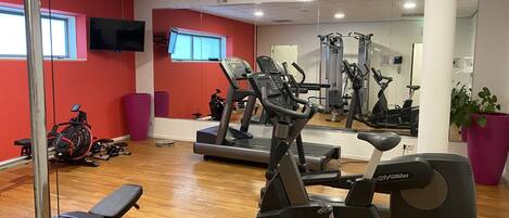 Une salle de sport équipée de machines de cardio, d’un banc et d’un grand miroir.