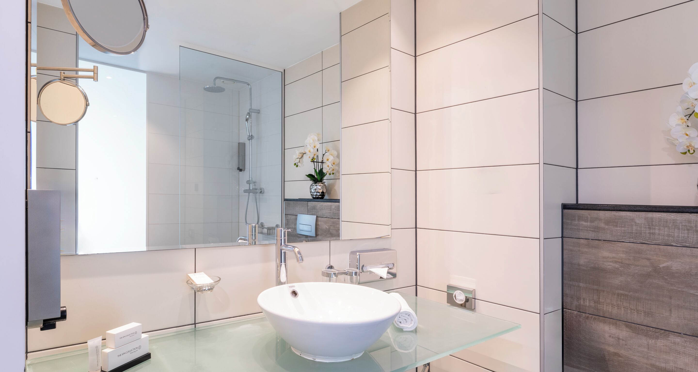 Une salle de bain moderne avec un lavabo en verre, un grand miroir et une douche.