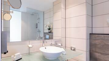 Une salle de bain moderne avec un lavabo en verre, un grand miroir et une douche.