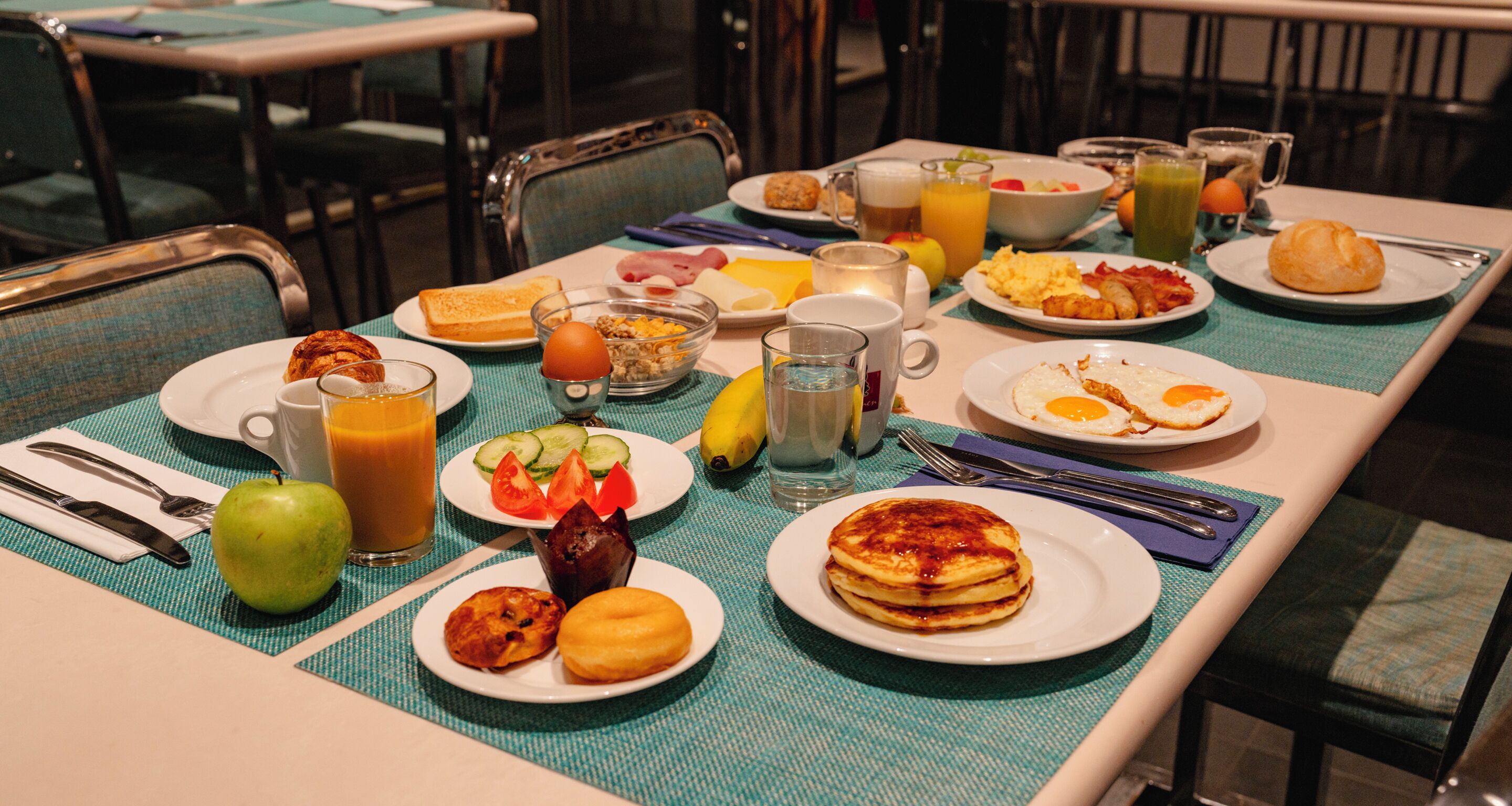 Un bufé de desayuno con diversos platos, bebidas y un bol de fruta.