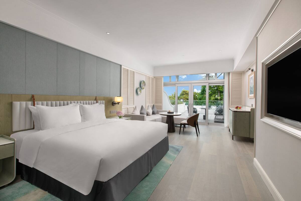 Een moderne hotelkamer met een groot bed, een zithoek met een tafel en stoelen, en een groot raam met uitzicht op het omliggende landschap.