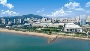 Vista aérea de una ciudad costera con un estadio grande, edificios altos y una playa.