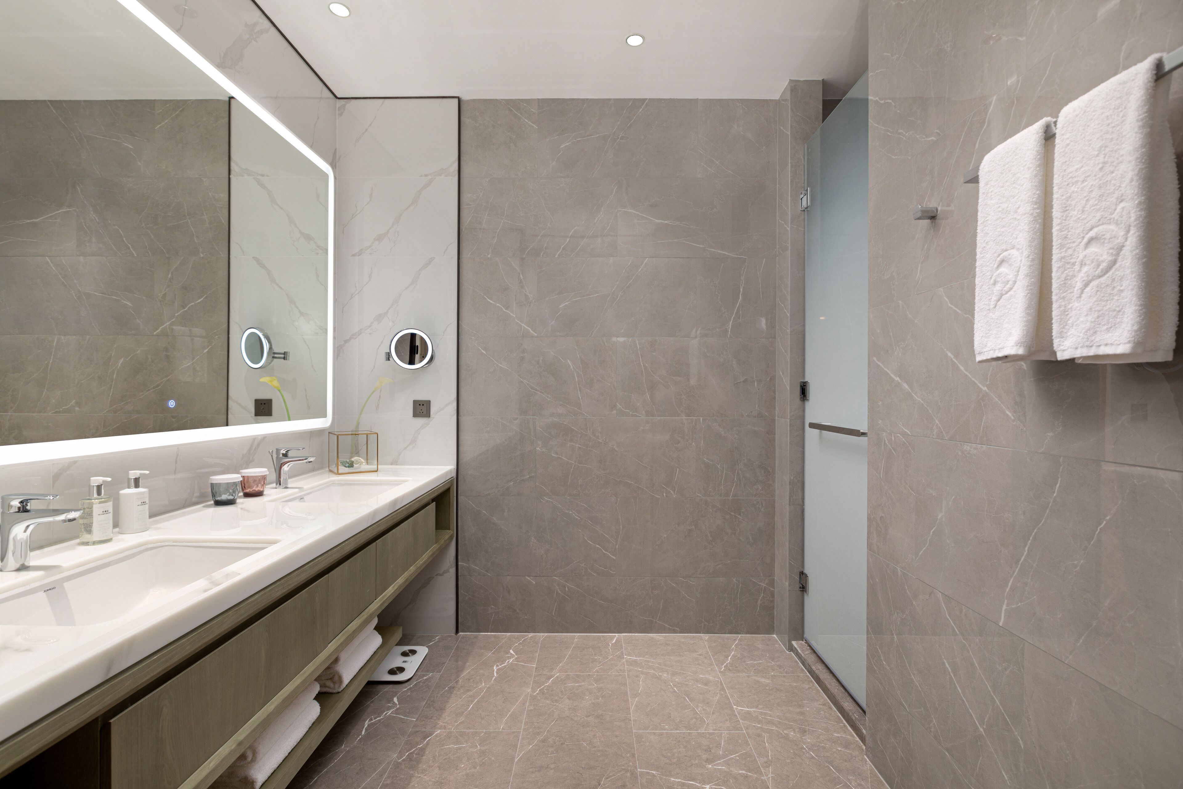A modern bathroom with a large mirror, two sinks, a shower, and a towel rack.