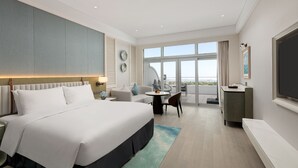 Una habitación de hotel moderna con una cama grande, un balcón con vistas, una pequeña zona de comedor y un televisor.