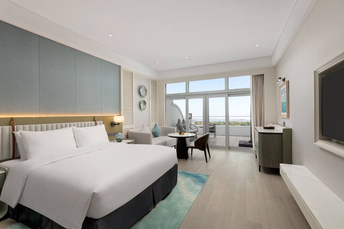Een moderne hotelkamer met een groot bed, een balkon met uitzicht, een eethoekje en een televisie.