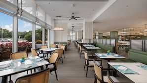 Un restaurante espacioso con techos altos, ventanas amplias y diferentes opciones de asientos, como mesas y cabinas.