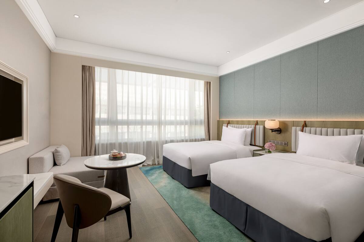 Een hotelkamer met twee bedden, een bank, een bureau en een groot raam met gordijnen.
