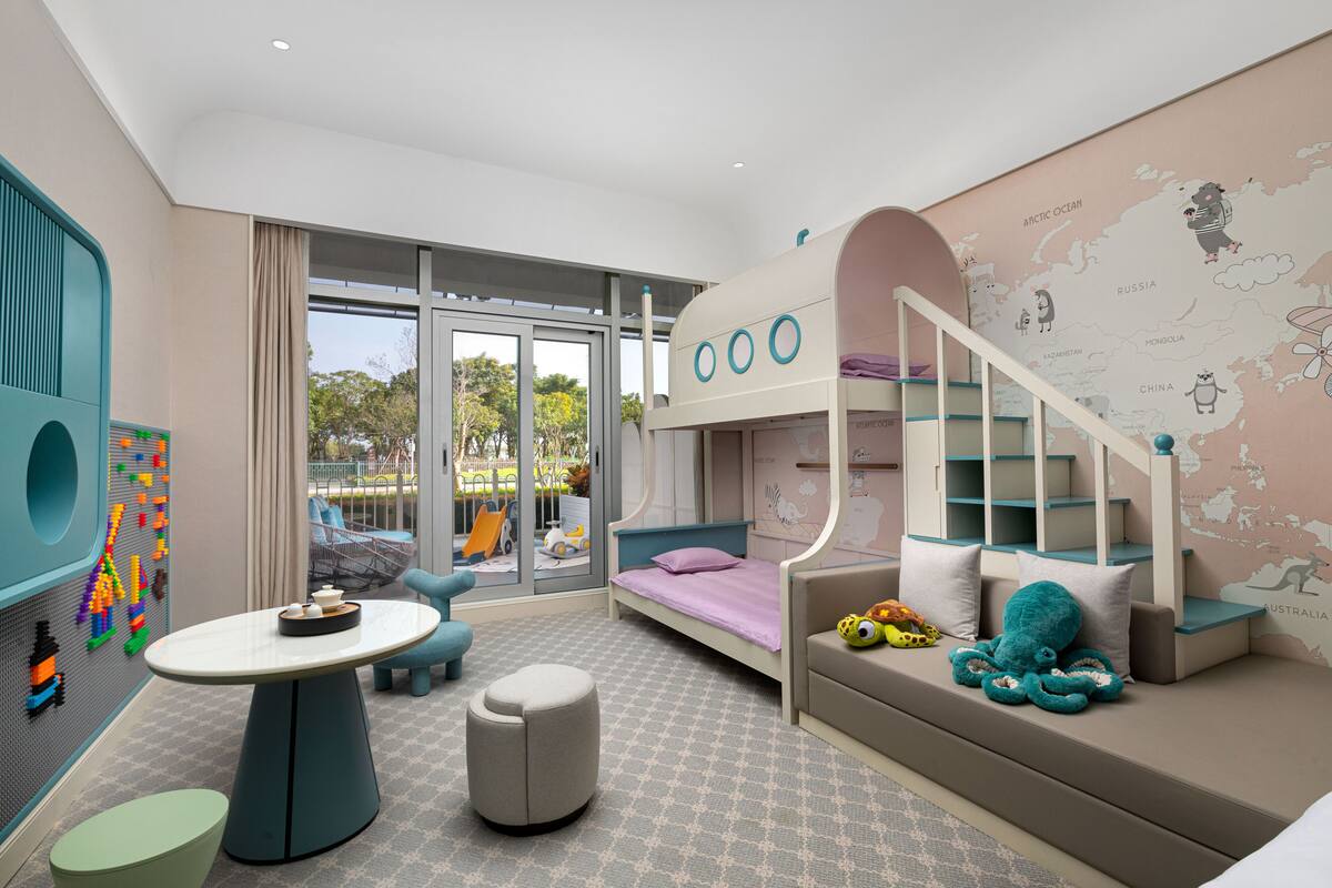 Een kinderkamer met een stapelbed, een speelhoek vol speelgoed en een groot raam.