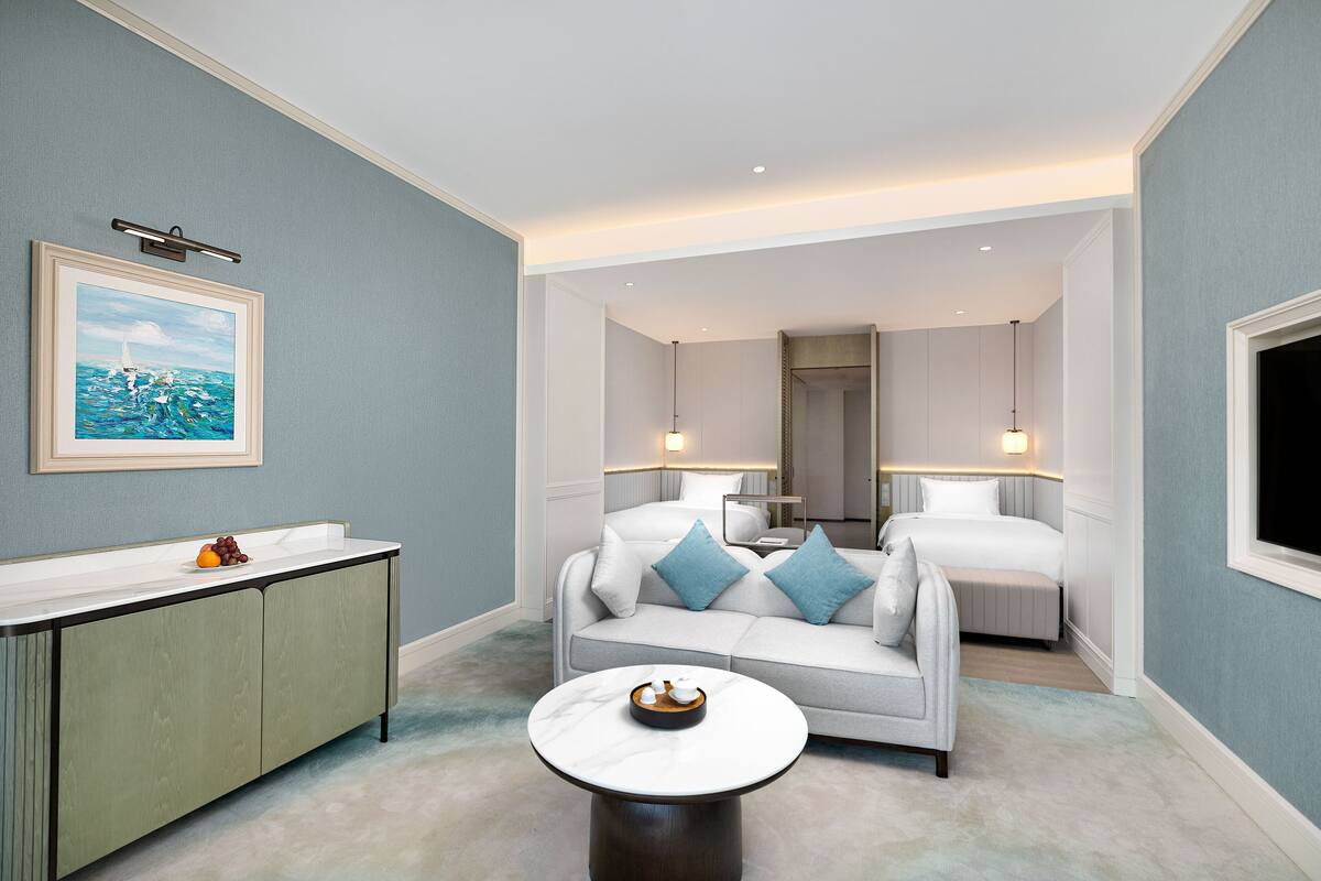 Een moderne hotelkamer met een witte bank, een klein rond tafeltje, een grijze kast en een schilderij aan de muur.
