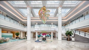 A spacious lobby with high ceilings, a central decorative light fixture, a staircase, and a reception area.